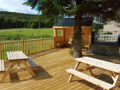 una terraza de madera con 2 mesas de picnic y un árbol en Carn Mhor Bed and Breakfast, en Aviemore