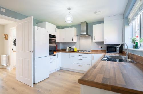 a kitchen with white cabinets and a white refrigerator at Immaculate 4-Bed House 5mins walk to Village shop in Bicester