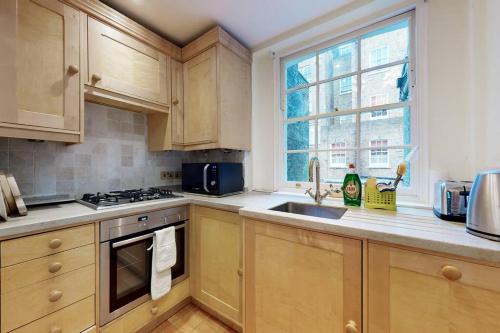 uma cozinha com armários de madeira, um lavatório e uma janela em Lovely 1 bedroom flat in Pimlico em Londres