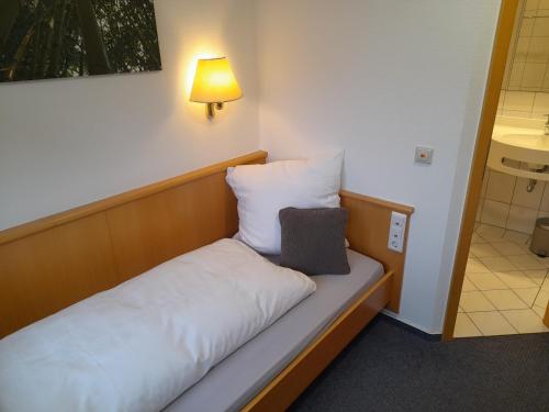a small bed in a room with a light on the wall at Hotel Zurmühlen in Sendenhorst