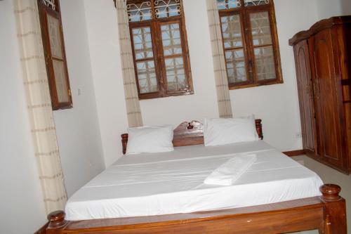 a bedroom with a bed with white sheets and windows at SULKHAN SERVICED APARTMENT in Chukwani