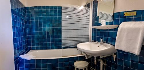 een blauw betegelde badkamer met een wastafel en een bad bij Hotel Le Boischaut - Citotel Chateauroux in Châteauroux