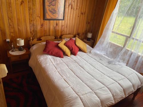 a bedroom with a bed with red and yellow pillows at Cabañas Campestres Villarrica in Villarrica