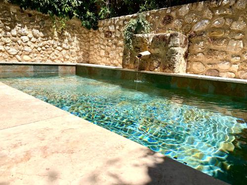 une piscine avec un mur en pierre et une fontaine dans l'établissement La Maison du Courtil, Amande-Olive, à Moustiers-Sainte-Marie