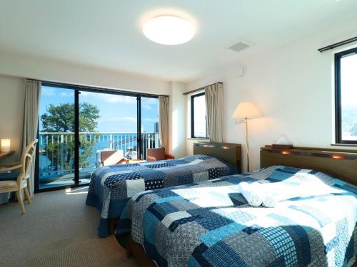 two beds in a hotel room with a balcony at Izu Kansya in Atami