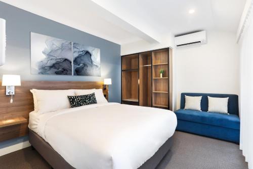 ein Schlafzimmer mit einem weißen Bett und einem blauen Sofa in der Unterkunft Killara Hotel & Suites in Killara