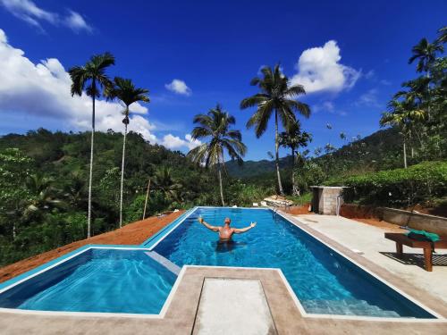 a man in a swimming pool with palm trees in the background at Rainforest Mount Lodge in Deniyaya