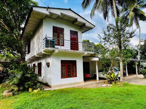 een wit huis met rode deuren en een tuin bij Summer Ridge - Homestay in Ratnapura