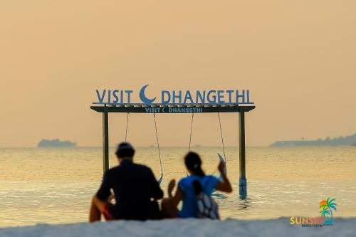 two people sitting on the beach in the water at Sunset Beach View in Dhangethi