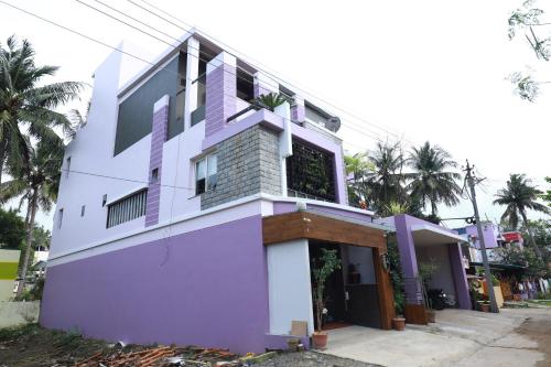 a purple and white building with palm trees at The Ideal Nest Kumbakonam in Kumbakonam