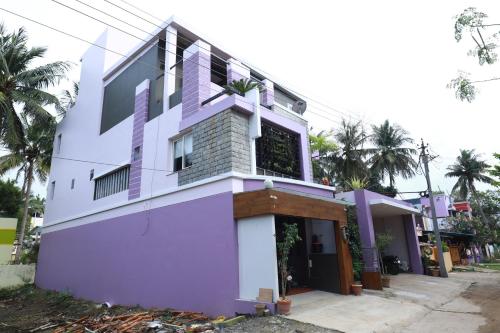 a purple and white house with palm trees at The Ideal Nest Kumbakonam in Kumbakonam