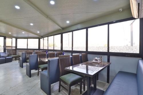 a dining room with tables and chairs and windows at Hotel Merit in Surat