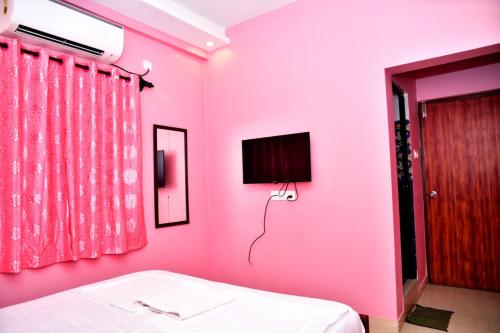 Habitación de color rosa con cama y TV en INDRAYANI GUEST HOUSE en Calangute