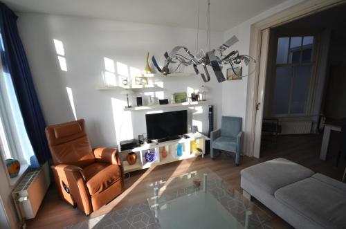 a living room with a tv and a chair and a couch at Fraai appartement direct aan zee op toplocatie. in Vlissingen