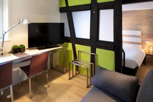a room with a desk with a television and a bed at Hotel Le Colombier Suites in Colmar