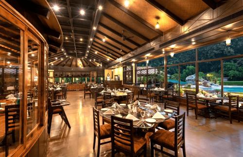 a dining room with tables and chairs and windows at Aahana The Corbett Wilderness in Rāmnagar