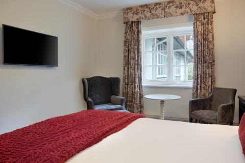 a bedroom with a bed and two chairs and a tv at Sunday Box Hill Burford Bridge Hotel in Dorking