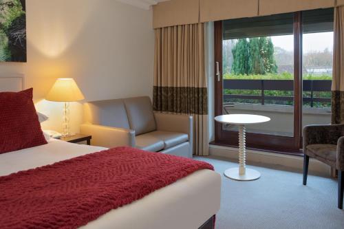 a hotel room with a bed and a chair and a window at Sunday Box Hill Burford Bridge Hotel in Dorking