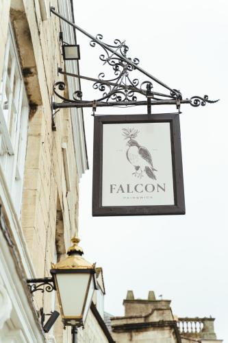 a sign hanging on the side of a building with a lamp at The Falcon Inn in Painswick