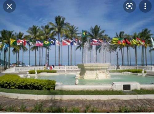 a fountain with palm trees and flags in front of the ocean at Apartamento para temporada Ambiente familiar in Santos