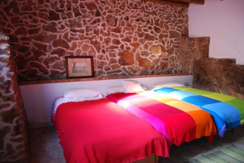 Cama colorida en habitación con pared de piedra en CASA DE DOÑA MARIA VALDELARCO, en Valdelarco