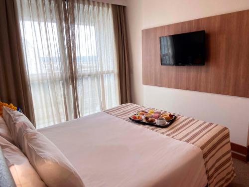 a hotel room with a tray of fruit on a bed at Athos Bulcão Hplus Executive in Brasilia