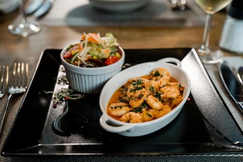 a black plate with a bowl of shrimp and a salad at Hotel & Restaurant Tanne in Fischingen