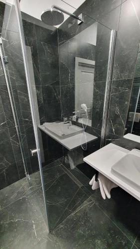 La salle de bains est pourvue de carrelage noir, d'un lavabo et d'une douche. dans l'établissement Apartamenty SIENKIEWICZA 8, à Żywiec