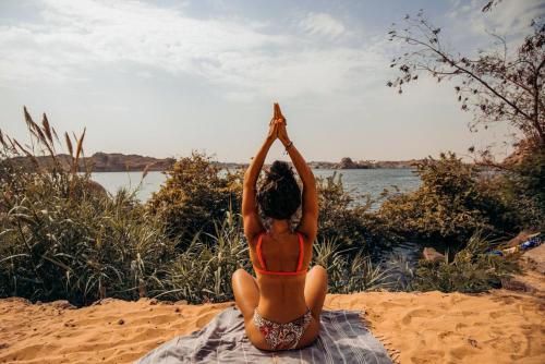 a woman in a bikini sitting on the beach doing a yoga pose at Eco Nubia in Aswan