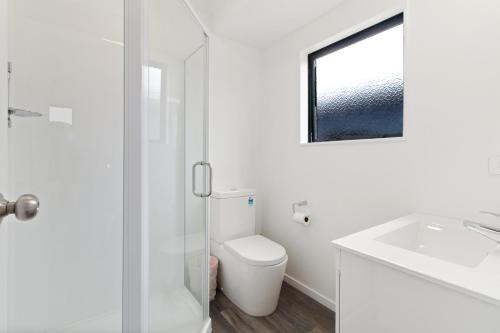 a white bathroom with a toilet and a sink at Sandy Shores - Waihi Beach Holiday Home in Waihi Beach