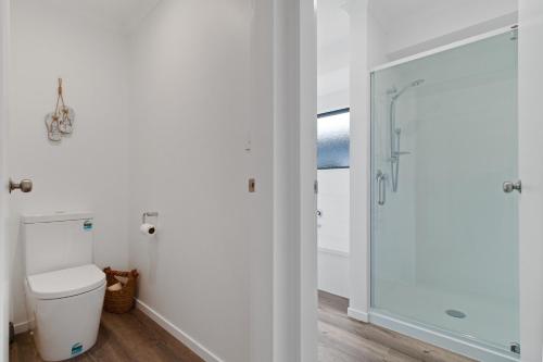 a bathroom with a toilet and a glass shower at Sandy Shores - Waihi Beach Holiday Home in Waihi Beach