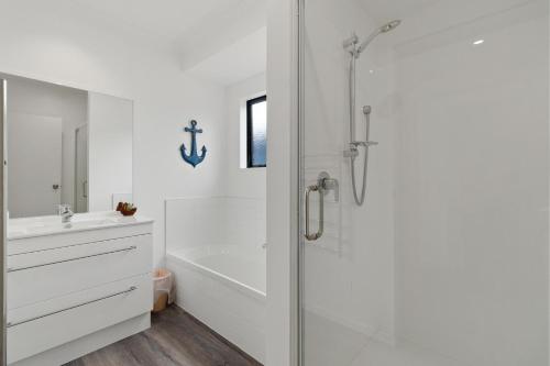 a white bathroom with a shower and a sink at Sandy Shores - Waihi Beach Holiday Home in Waihi Beach