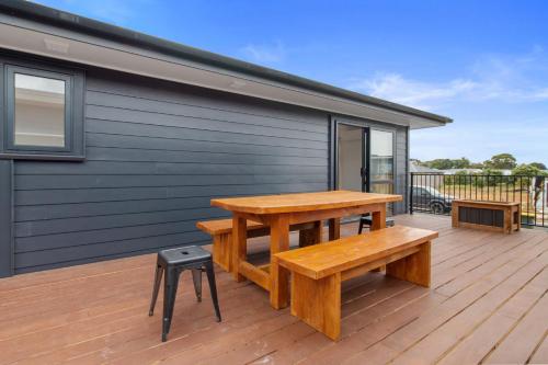 a wooden deck with a picnic table and a stool at Sandy Shores - Waihi Beach Holiday Home in Waihi Beach