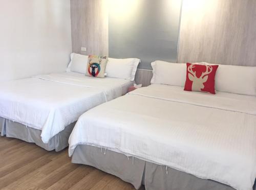 in墾丁 في كنتيج: سريرين في غرفة مع ملاءات بيضاء ووسائد حمراء