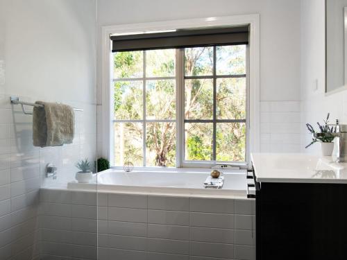 a white bathroom with a tub and a window at Lucini Cottage in Hepburn Springs