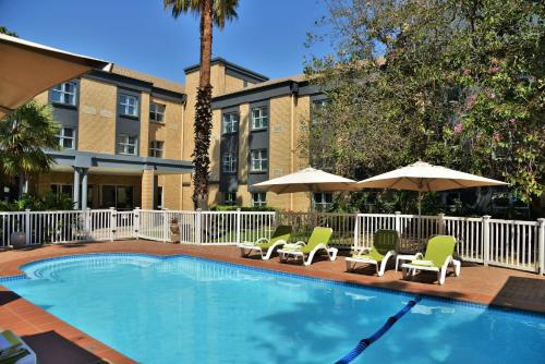 a swimming pool with lounge chairs and umbrellas at Holiday Inn Johannesburg Airport, an IHG Hotel in Kempton Park