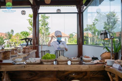 a person wearing a mask standing behind a counter with food at Cantho Eco Resort in Can Tho