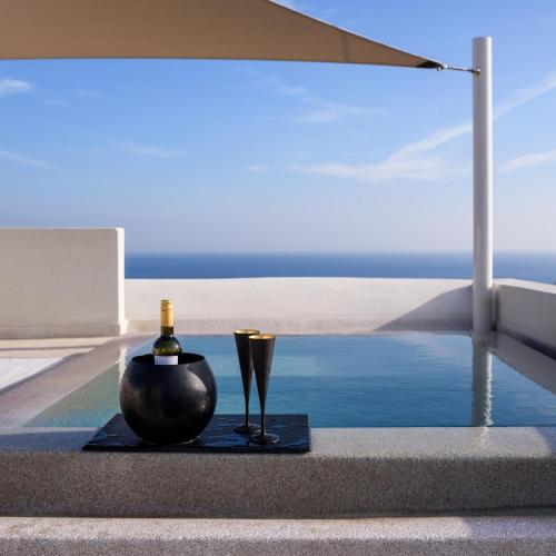 a bottle of wine and a glass next to a pool at Potnia Theron Suites in Akrotiri