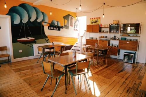 a dining room with tables and chairs and a kitchen at The Dolphin Inn Hostel in Dunbar