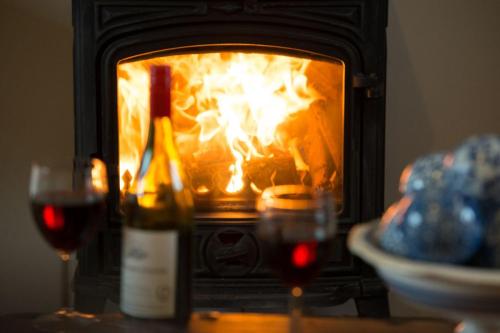 a bottle of wine and two glasses of wine in front of a fireplace at The Stables, relax in 5 star style and comfort with lovely walks all around in Great Maplestead