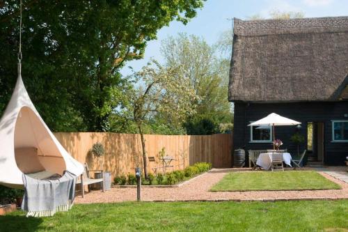 a yard with a fence and a house with a tent at Deepwell Granary is a lovely thatched barn with attached meadow woodland in Buxhall
