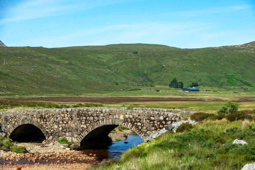 a stone bridge over a river in a field at Kinloch Ainort Apartments in Luib