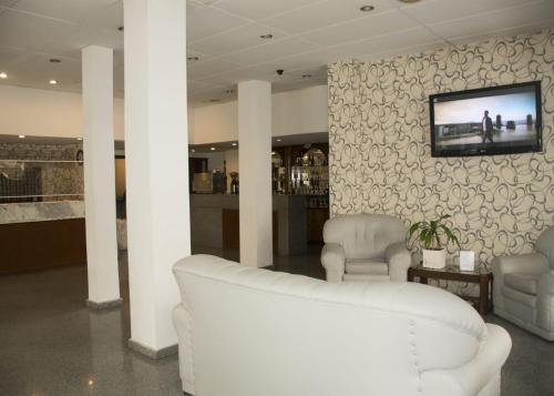 a living room with two white chairs and a tv on a wall at Gran Hotel Manila in Mar del Plata