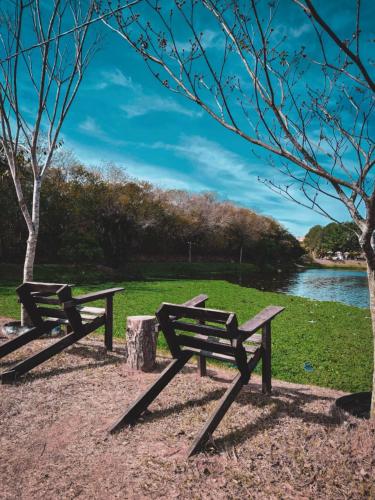 two picnic benches sitting next to a river at Pousada e Camping Carrion in Itu
