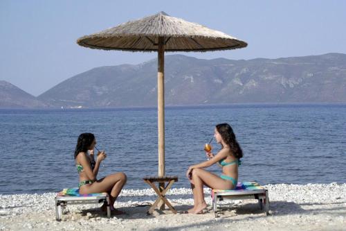two women in bathing suits sitting under an umbrella on the beach at Sami Beach Hotel in Sami