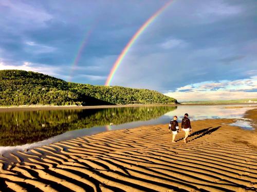 two people walking on the beach with a rainbow in the background at Le Relais de la Martine in Petite-Rivière-Saint-François
