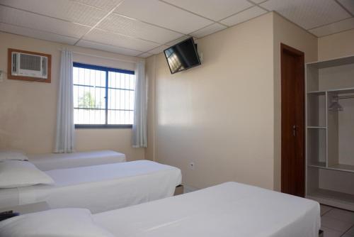 a room with two beds and a tv on the wall at Lord Hotel Camburi in Vitória