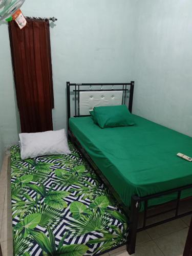a bed with a green comforter and a pillow at Sella Guest House in Banyuwangi