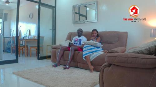 a man and a woman sitting on a couch at The View Apartments in Brusubi