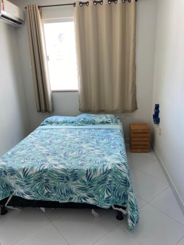 a bedroom with a bed with a blue comforter and a window at Apto Praia do Amor 2 quatos in Conde